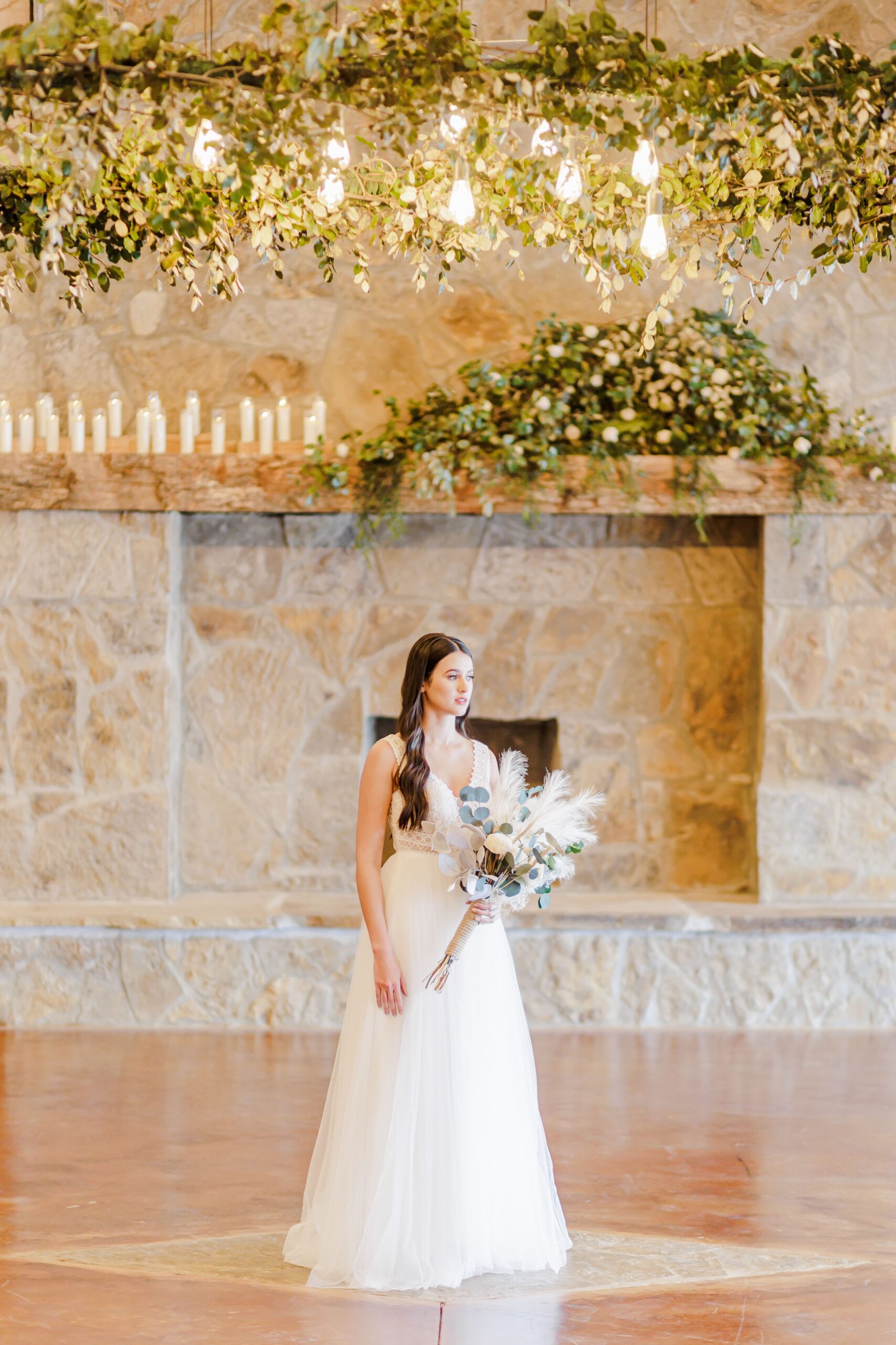 A beautiful bride stands in the middle of a decorated room holding a bouquet of flowers. 