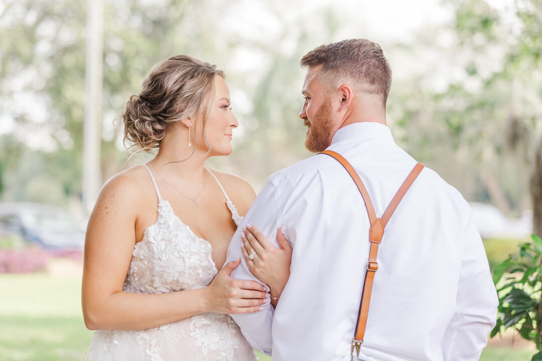 A bride holds on to the arm of her new husband who is wearing tan suspenders and a white shirt