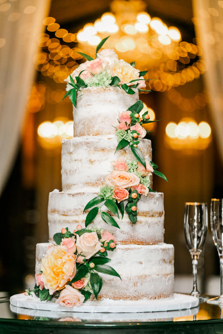 Details of a wedding cake with pink flowers in front of a crystal chandelier